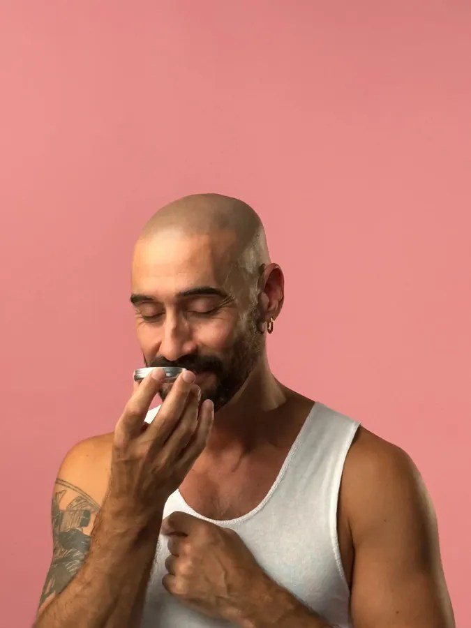Man smelling an open tin of No Pong natural deodorant on a pink background